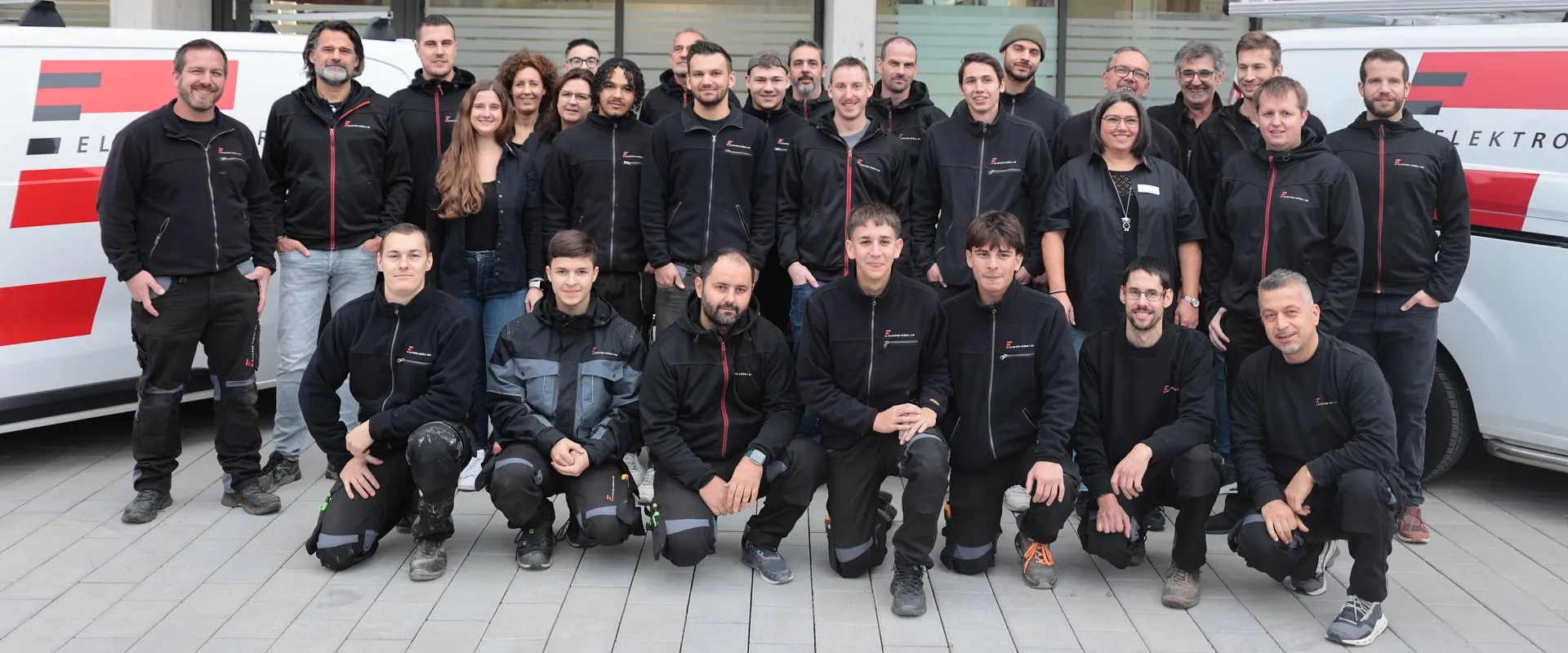Das Team der Elektro Fröhli AG in Arbeitskleidung vor den Firmenfahrzeugen